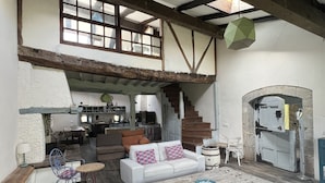 A rustic interior with exposed wooden beams, a loft bedroom, a dining area, and a kitchen.