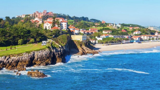 A coastal town with buildings on a hillside, a beach, and rocky cliffs.