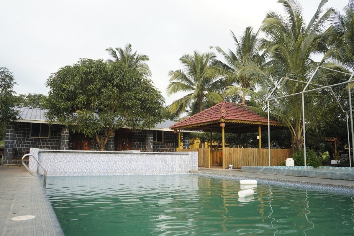 Una piscina con borde de azulejos, un quiosco de madera y palmeras al fondo.
