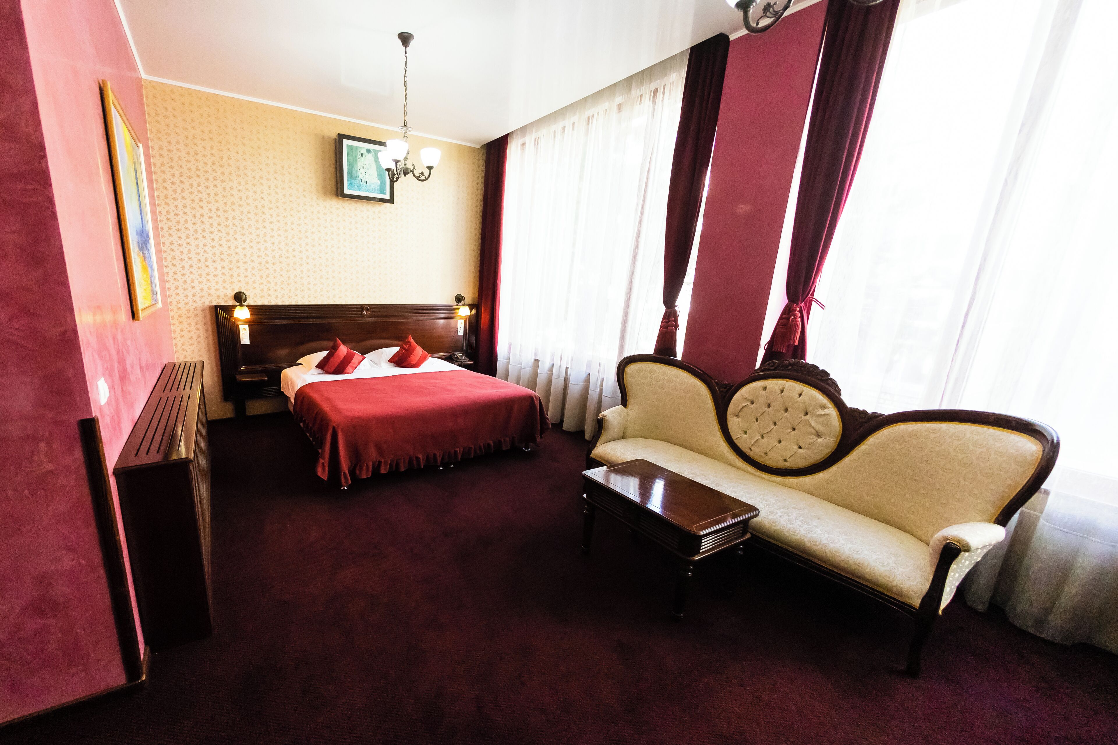 A hotel room with a bed, a sofa, a nightstand, and a chandelier.