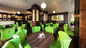 Un restaurant avec des chaises à revêtement vert, des tables en bois et des luminaires suspendus.
