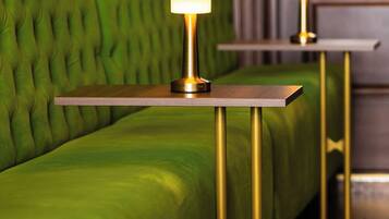 A green upholstered sofa with a tufted backrest and two bedside tables with gold legs and illuminated lamps.
