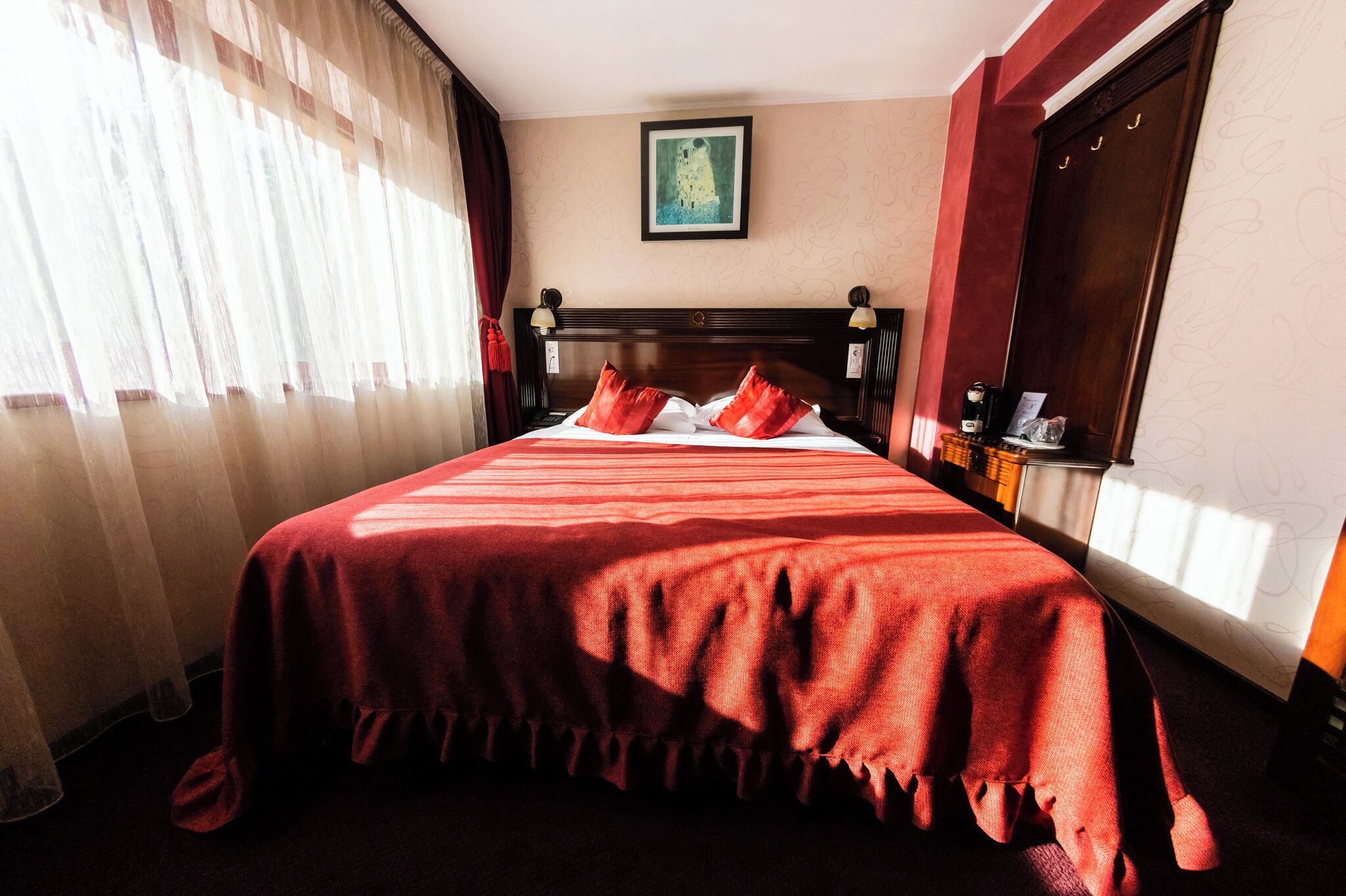 Una habitación de hotel con una cama grande, una mesita de noche con lámpara, una ventana con cortinas y un cuadro en la pared.