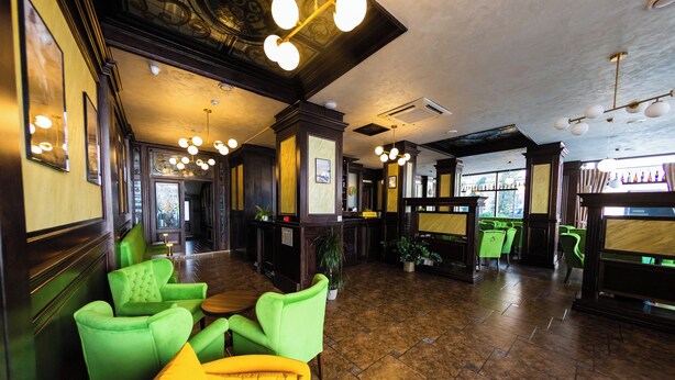 Un hall d’entrée avec des sièges verts et jaunes, des panneaux de bois et un espace bar avec des chaises vertes.