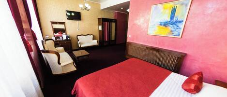 Una habitación de hotel con una cama grande, un escritorio con una silla, un televisor y un cuadro en la pared.