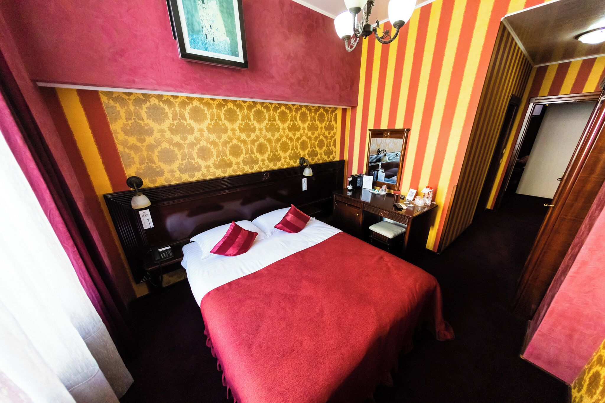 A hotel room with a large bed, a nightstand, a dresser, and a mirror.