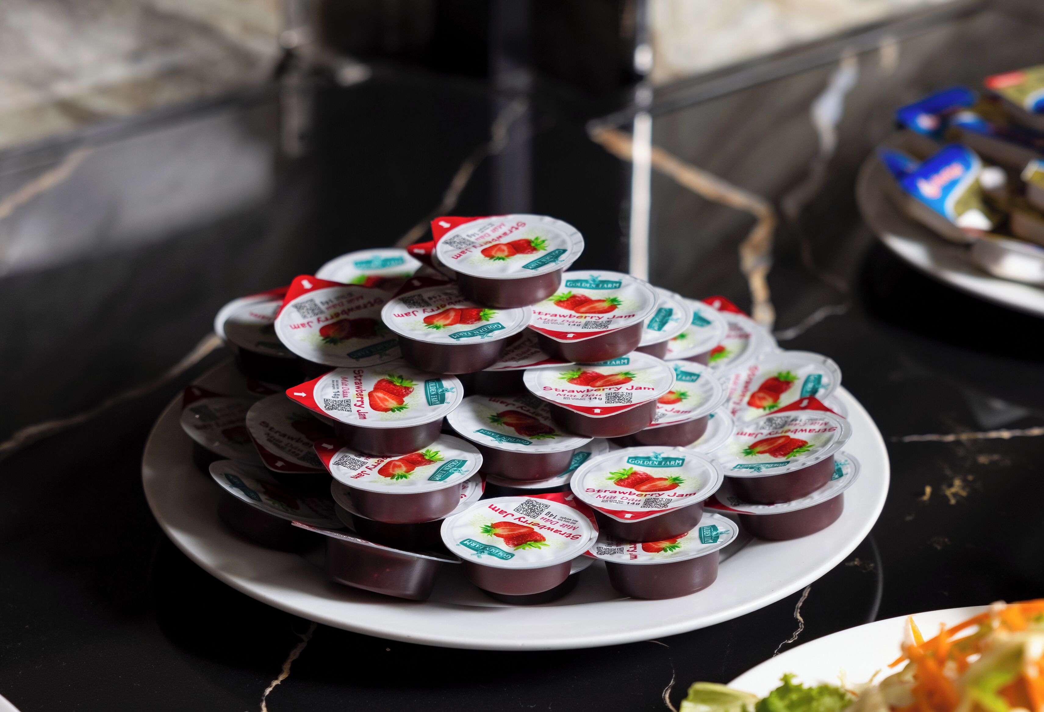 Une assiette remplie de pots de confiture de fraises, disposés en pyramide sur une table.