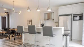 Una cocina moderna con armarios blancos, electrodomésticos de acero inoxidable y una isla central con taburetes.