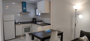 A compact kitchen with a stove, oven, and a coffee maker. There is a dining table with chairs and a small table lamp. - APARTAMENTO ENTRE SALINES Y PLAYA (Calpe)