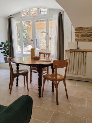 Un coin repas avec une table ronde en bois, quatre chaises, une plante en pot et, à travers une porte vitrée, une vue sur un espace extérieur.