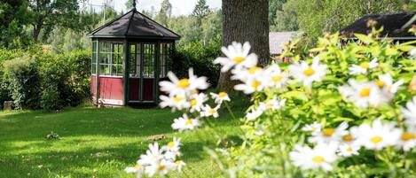 A gazebo in a garden with a large tree and blooming flowers.