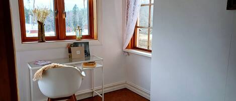 A room with a desk, chair, and a window with lace curtains.