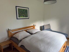 Ein Schlafzimmer mit einem hölzernen Bett, einem Nachttisch, einem Beistelltisch, einem Stuhl und einem gerahmten Bild an der Wand.