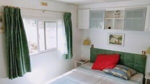 Een slaapkamer met een bed, groene gordijnen, een raam, een hoofdeinde en een nachtkastje.