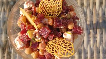Un tazón de ensalada con garbanzos, tomates en cubos y una celosía amarilla decorativa sobre una superficie tejida.