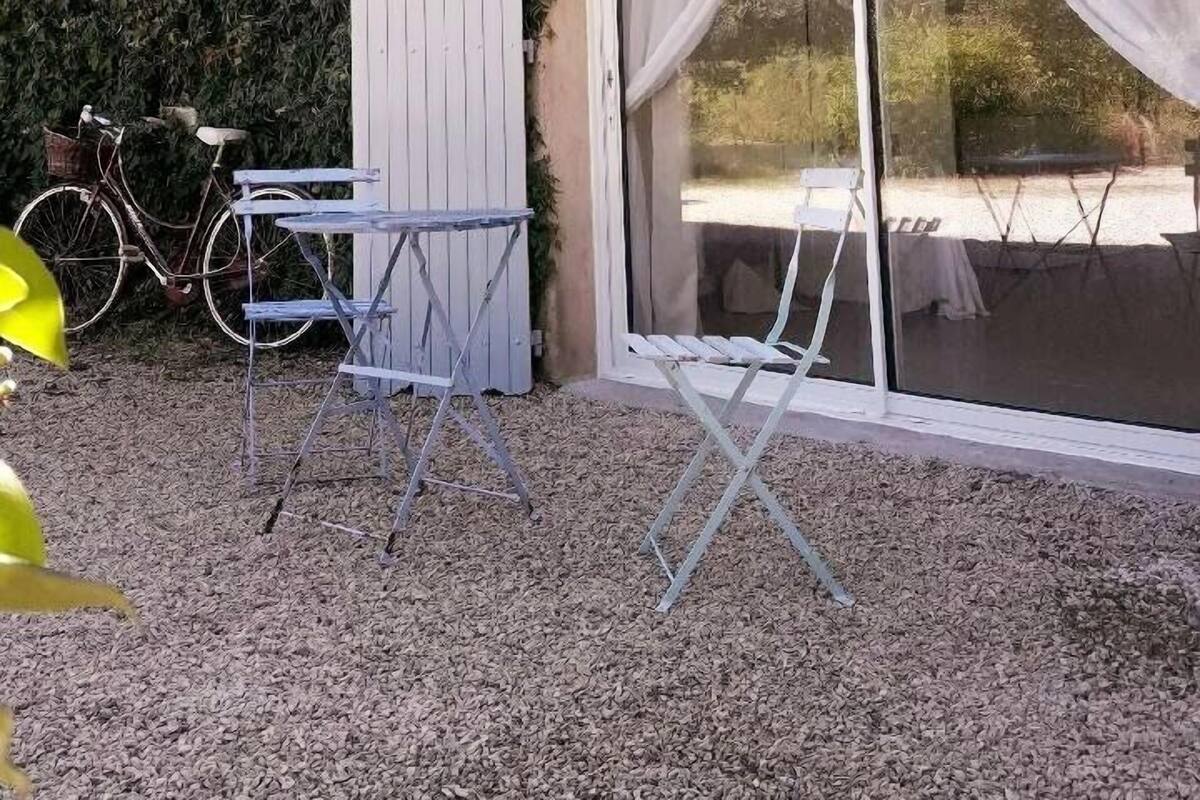 A patio area with a table and chairs, a bicycle, and a white door leading to a covered outdoor space.
