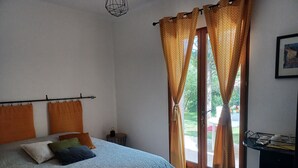 Een slaapkamer met een bed, oranje gordijnen, een klein tafeltje en uitzicht op het omliggende landschap.
