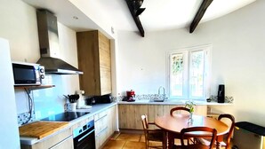 A compact kitchen with a wooden countertop, a built-in oven, a microwave, and a coffee maker. There is a dining table with chairs and a window with a view of greenery outside.