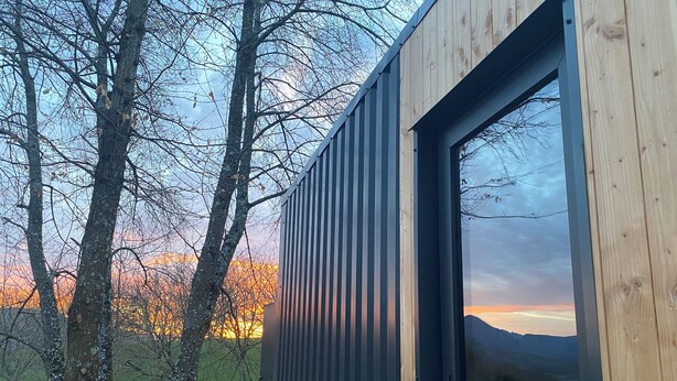 Un edificio moderno con un gran ventanal y vistas a un paisaje verde al atardecer.