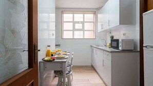 Une cuisine de taille réduite avec des meubles blancs, un four à micro-ondes et une fenêtre.