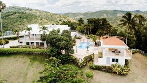 Una villa blanca con piscina, rodeada de exuberante vegetación y colinas.