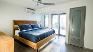 Un dormitorio con una cama de madera, un ventilador de techo y un ventanal corredizo al exterior.
