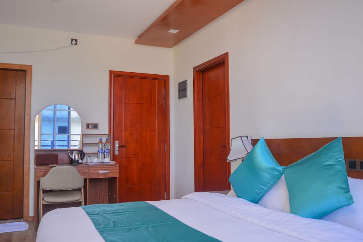 A hotel room with a bed, a desk, and a chair. There are wooden doors and a window with a view.