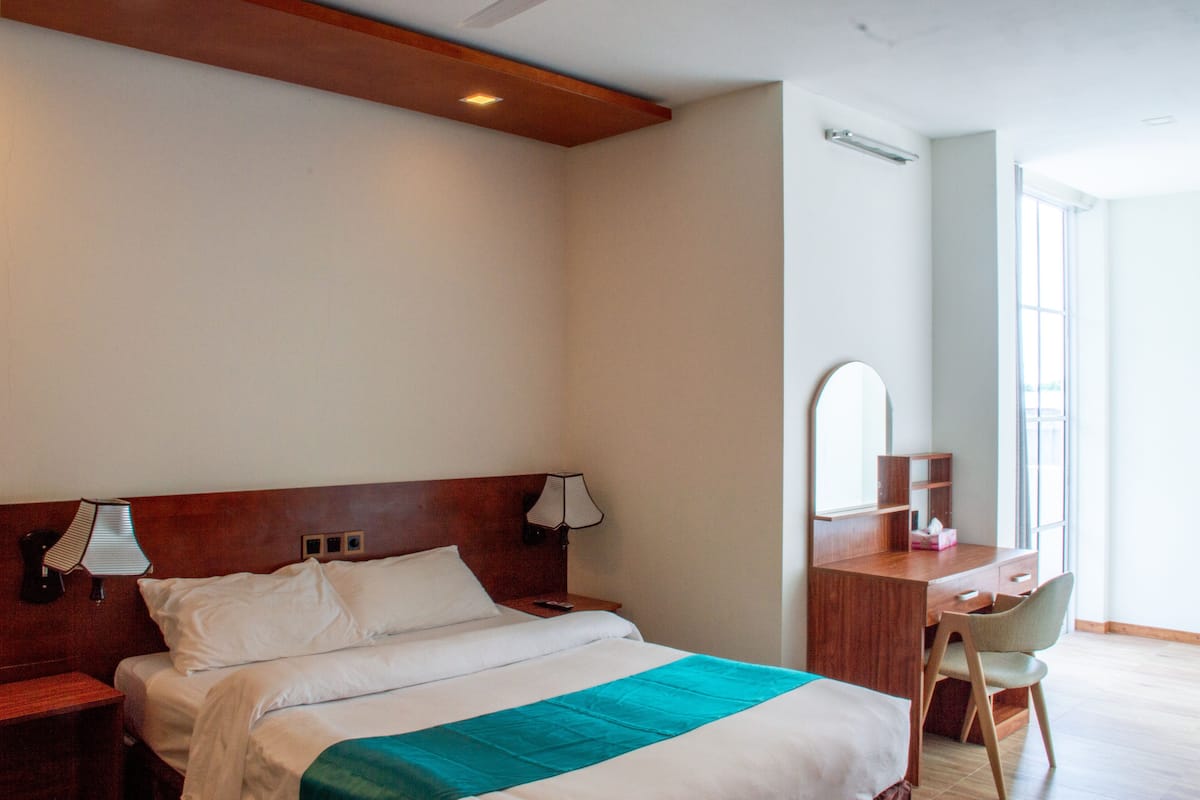 A hotel room with a bed, bedside tables, a desk with a chair, a mirror, and a window.