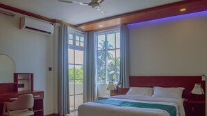 Habitación de hotel con cama, escritorio, silla y ventanas amplias.