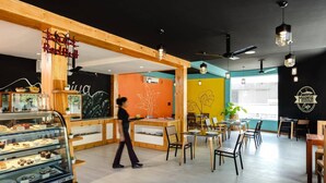 Interior de una cafetería moderna con detalles de madera, una barra mostrando pasteles y una zona de estar con mesas y sillas.