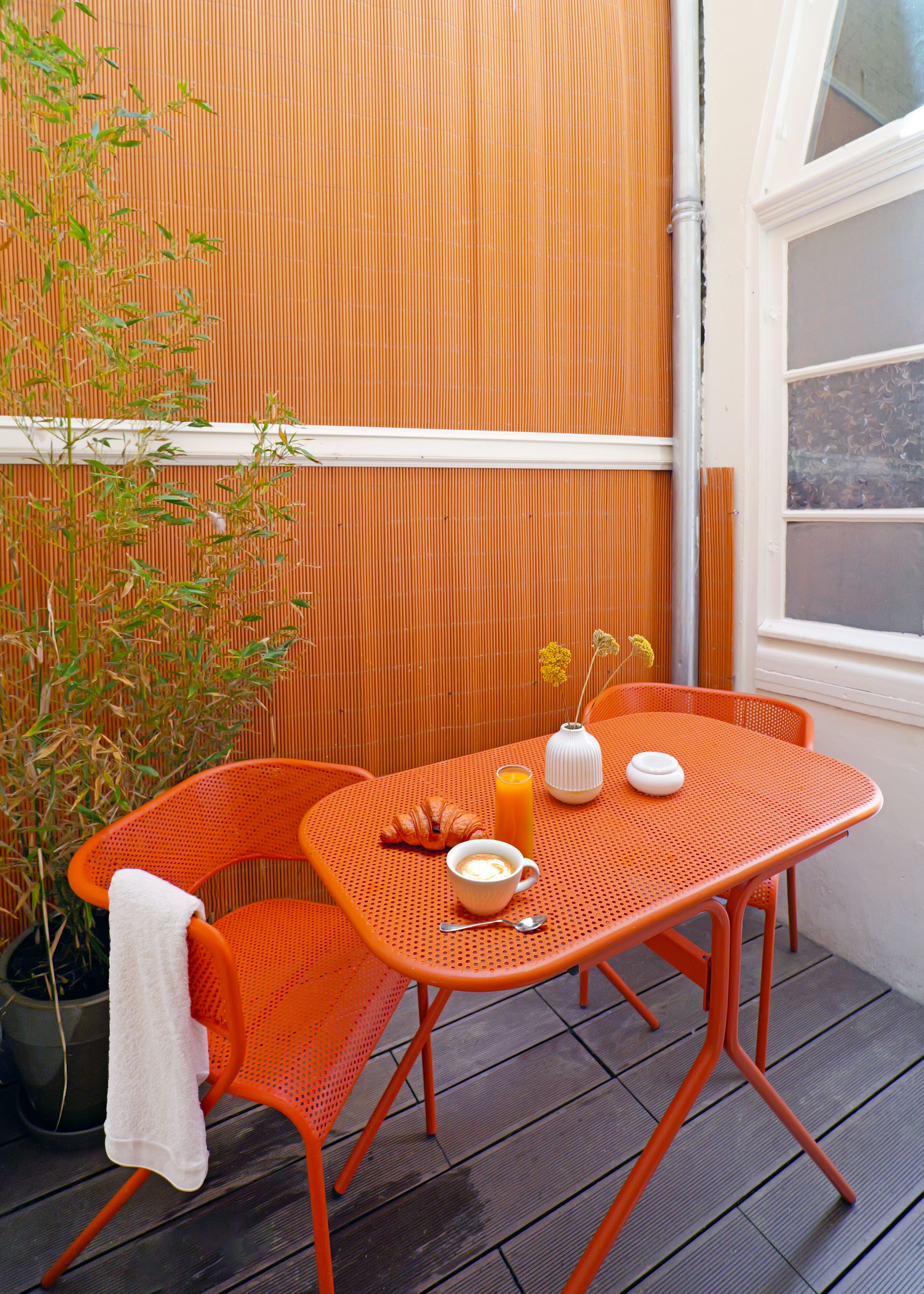 An outdoor dining area with a table and chairs, a potted plant, and a window.