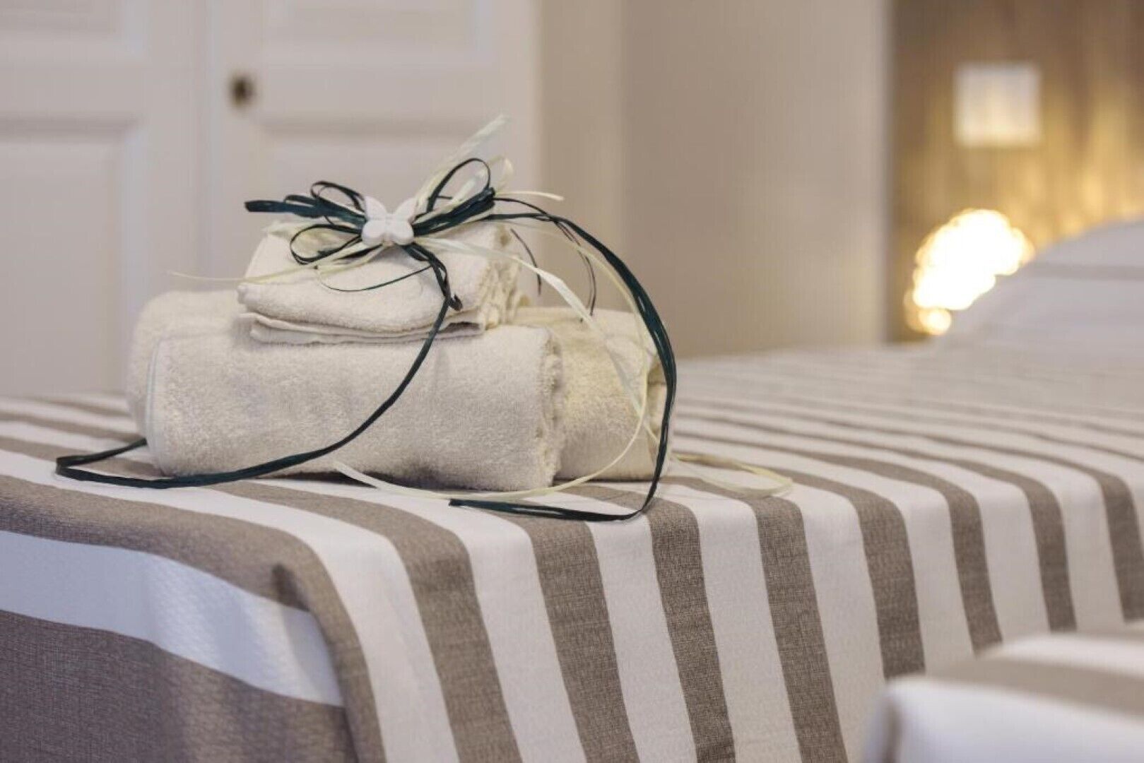A neatly made bed with striped bedding and a stack of folded towels tied with a bow.