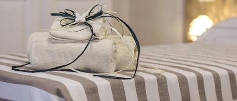 A neatly made bed with striped bedding and a stack of folded towels tied with a bow.