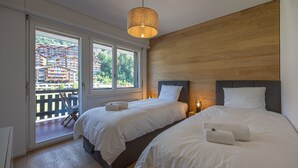 A hotel room with two beds, a wooden wall, and a balcony with a view of buildings. - Ecluses 6 - Nendaz centre & close to ski lift (Haute-Nendaz)