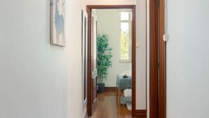Um corredor com piso de madeira, uma porta à direita e uma planta ao fundo.