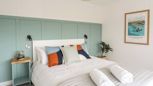 A neatly made bed with white linens, a teal headboard, and a framed picture of Pier Garth Bangor. - Dolwyn (Menai Bridge)