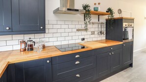 A modern kitchen with dark cabinets, a wooden countertop, a stainless steel range hood, and a built-in oven. - Dolwyn (Menai Bridge)