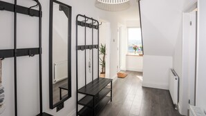 A hallway with a black metal rack, a mirror, a bench, and a hanging light fixture. - Dolwyn (Menai Bridge)
