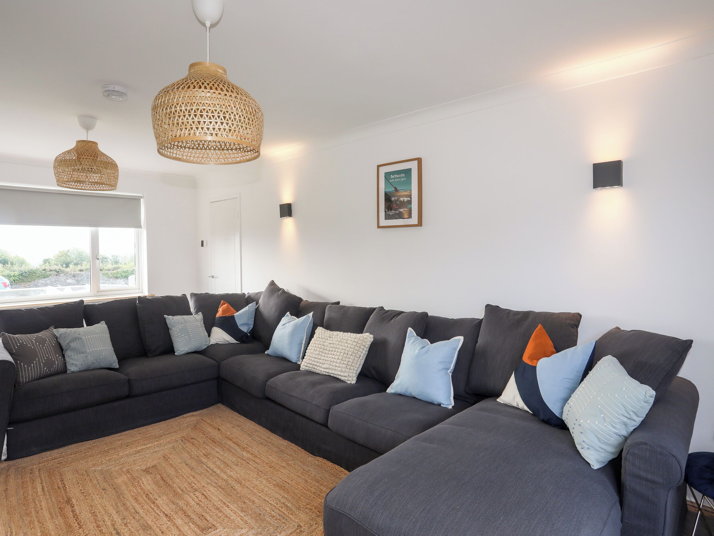 Una sala de estar moderna con un sofá modular, lámparas colgantes tejidas y un cuadro enmarcado en la pared.