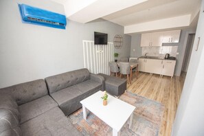 A modern living room with a grey sofa, a white coffee table, and a kitchen in the background. - PALVAN ACCOMMODATION (Antalya)