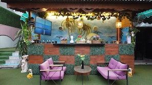 A cozy outdoor seating area with two purple chairs, a small round table, and a decorative wall with plants and a mural. - PALVAN ACCOMMODATION (Antalya)