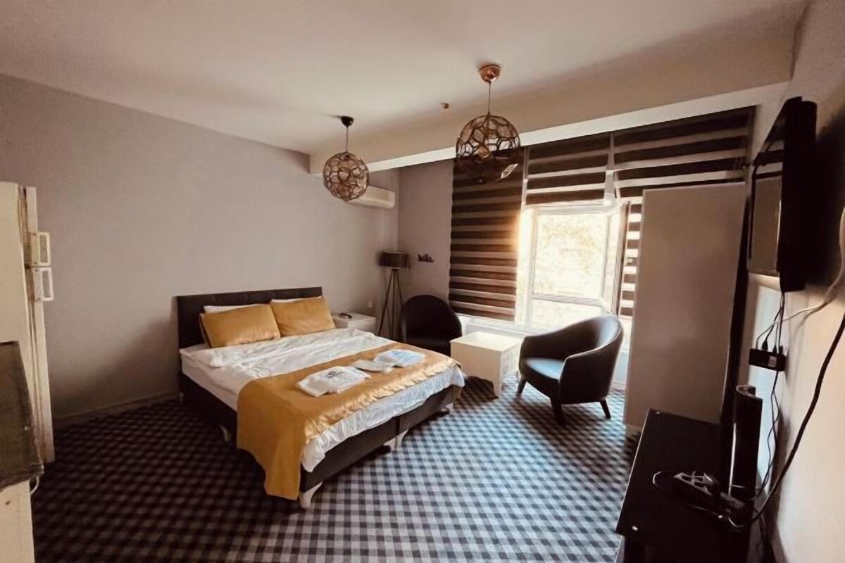 Habitación de hotel con cama, escritorio, silla, televisor y ventana con persianas.