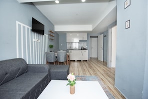 A modern living room with a grey sofa, a white coffee table with a vase, and a dining area with grey chairs. - PALVAN ACCOMMODATION (Antalya)
