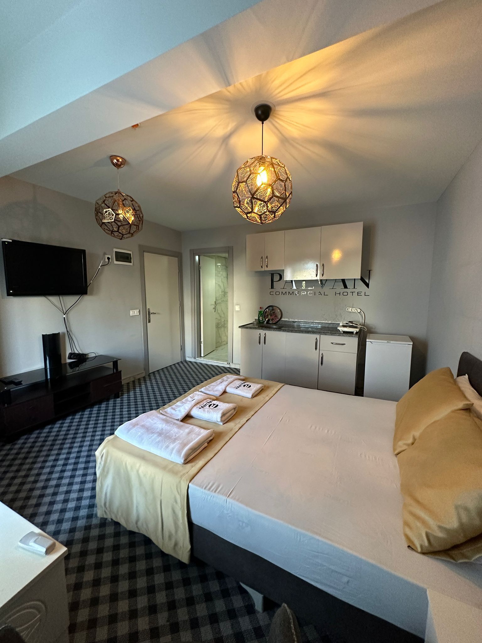 Een hotelkamer met een bed, een bureau, een televisie, een minibar en een plafondlamp.
