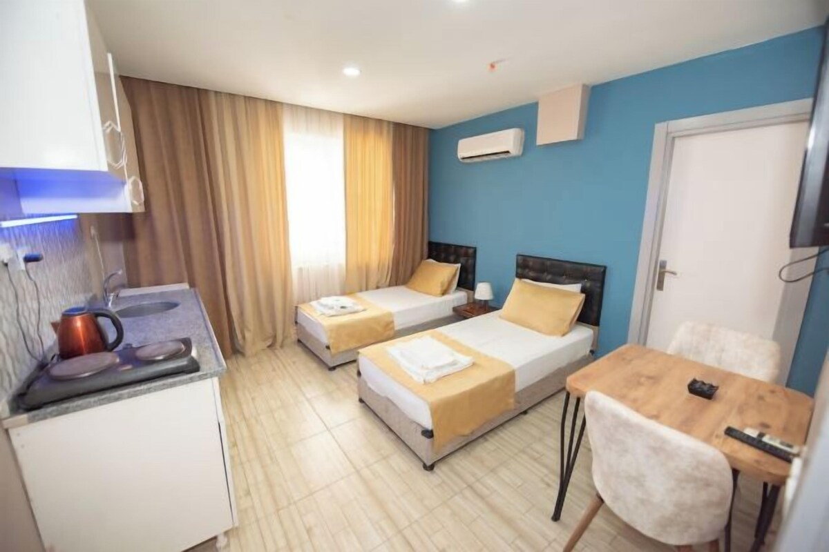 Habitación de hotel con dos camas, una kitchenette pequeña, una mesa de comedor y un televisor.