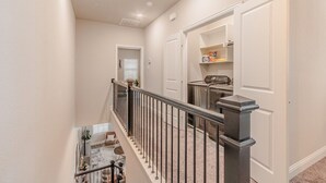 Un couloir avec un escalier, une porte dotée d’une étagère et un lave-linge.
