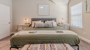 Une chambre à coucher avec un grand lit, deux tables de chevet, un tableau encadré au mur et une fenêtre avec des stores.