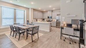 Une cuisine moderne dotée d’un îlot central, de meubles blancs et d’un coin repas avec une table et des chaises.