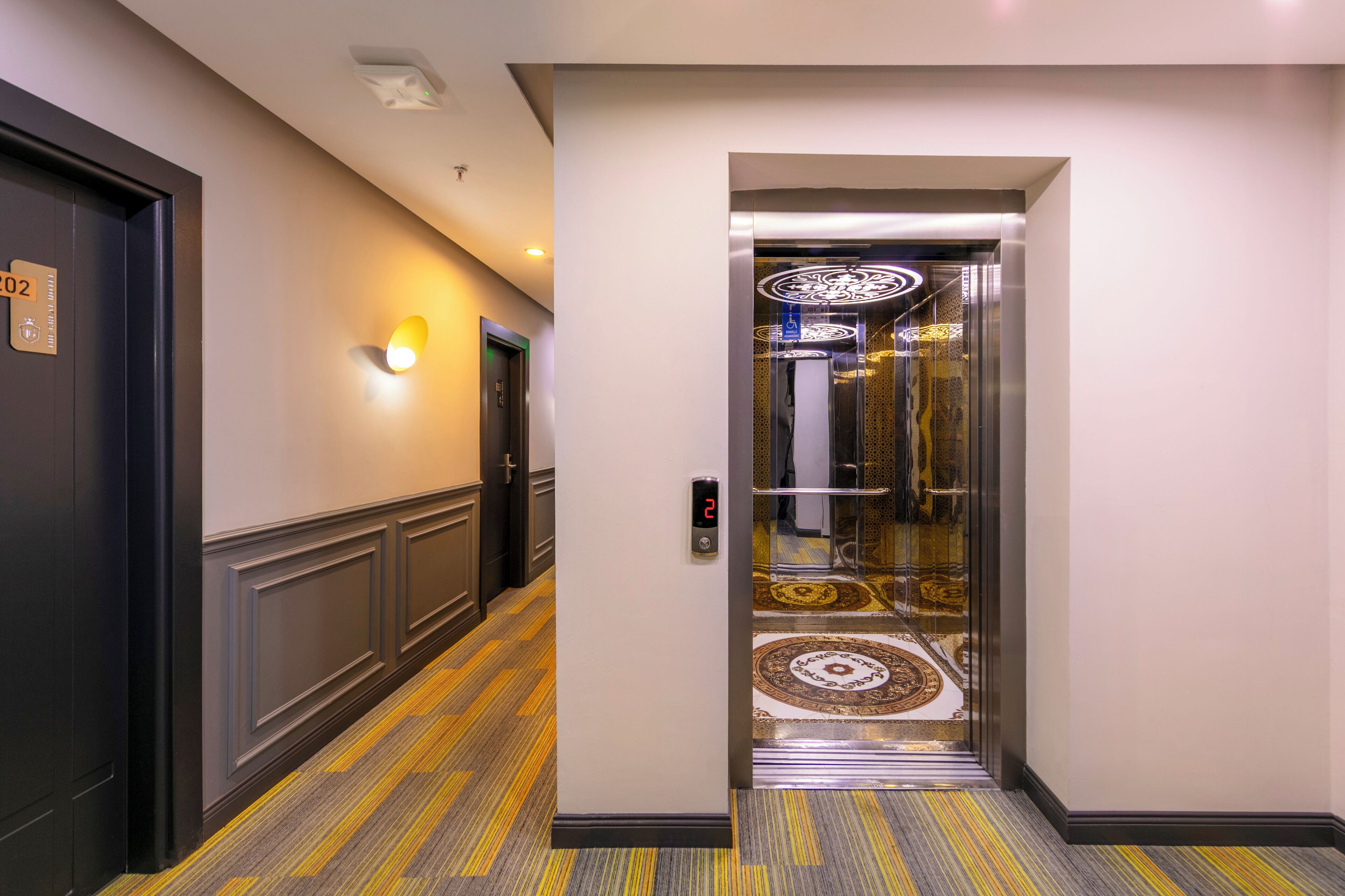 A hotel corridor with a carpeted floor, a door labeled "02", and an elevator with a digital display.