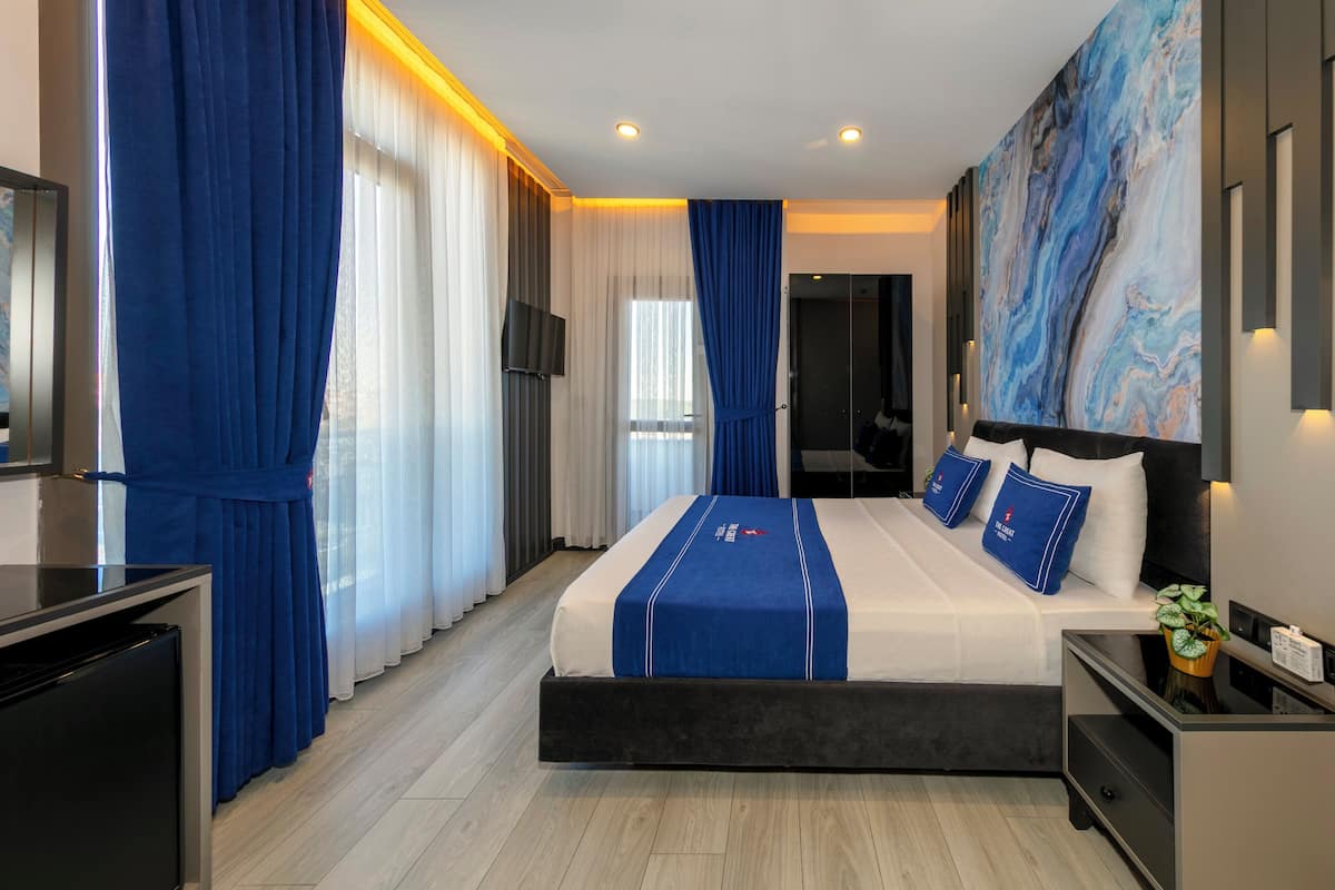 A modern hotel room with a large bed, a flat-screen TV, a desk, and a large abstract painting on the wall.